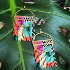 a pair of earrings with colorful beads hanging from it's sides on a plant