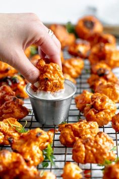 a person dipping some food into a small metal cup on a cooling rack with other foods