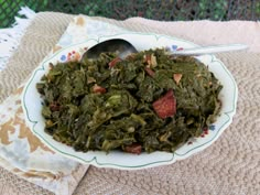 a white bowl filled with greens and bacon on top of a table next to a spoon