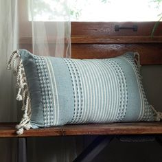 a blue and white striped pillow sitting on top of a wooden bench next to a window