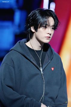 a young man with black hair and earphones on his head is standing in front of a colorful background