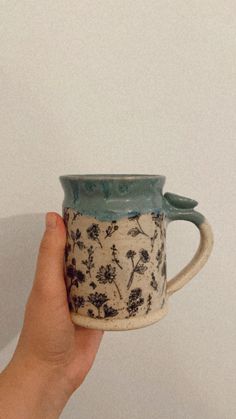 a hand holding a coffee cup with flowers on it, against a plain white wall