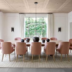 a dining room table with pink chairs and a vase on the centerpiece in front of a large window