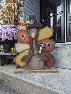 a wooden turkey sitting on top of a step next to flowers and cornucras