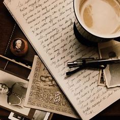 a cup of coffee sitting on top of an open book next to a pen and paper