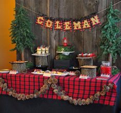 a table topped with lots of food next to a wooden fence covered in pine trees