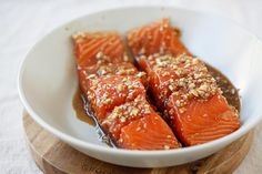 three pieces of salmon in a bowl with brown sauce and sesame sprinkled on top