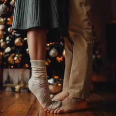 two people standing in front of a christmas tree with their feet on each other's legs