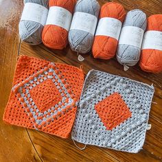 several balls of yarn sitting on top of a wooden table next to two crocheted squares