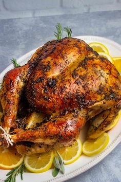 a whole chicken on a plate with lemons and rosemary