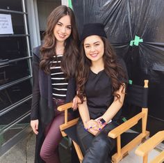 two young women sitting next to each other on a chair in front of a building