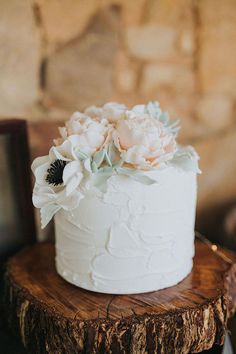 a wedding cake with white frosting and flowers on top sitting on a tree stump