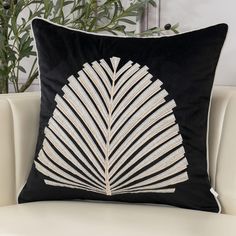 a black and white pillow with a decorative leaf design on the front, sitting on a couch