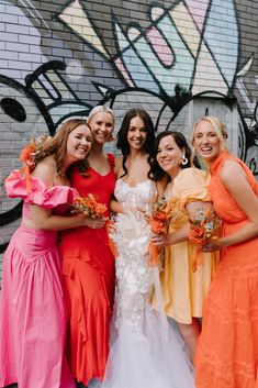 four bridesmaids pose for a photo in front of a graffiti - covered wall