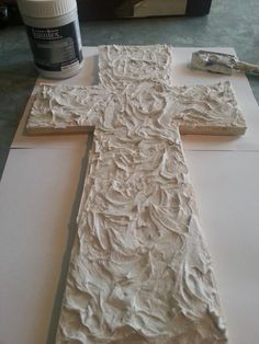 a cross made out of white paper on top of a table next to a can of paint