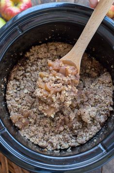 a wooden spoon is in an apple crockpot with oatmeal topping