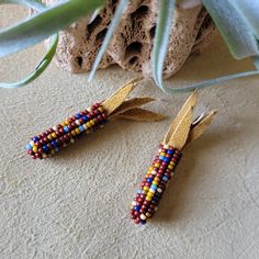 two pairs of beaded earrings sitting on top of a table next to a plant