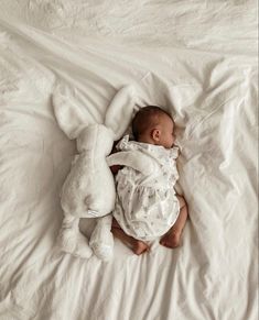 a baby laying on top of a white bed next to a stuffed animal bunny rabbit