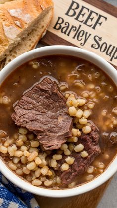 a bowl of beef barley soup with bread on the side