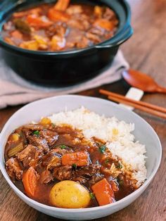 a bowl of stew with rice and carrots next to a pot of stew on a wooden table