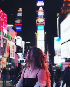 a woman standing in the middle of a busy city street at night with neon signs all around her