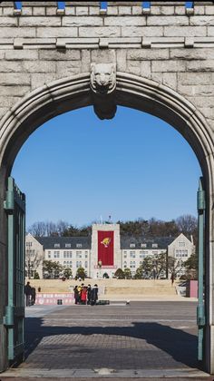 an archway leading to a building with a red flag on the top and people walking underneath it