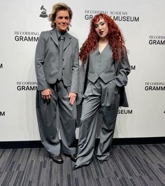 two people in suits standing next to each other on a carpeted floor with a wall behind them