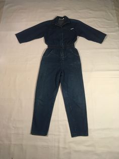 "vintage 80s women's denim jumpsuit label- Dreams cotton blue jeans wide smocked elastic waist chevron chest 2 hand pockets tapered leg good vintage condition, light wear a few faded stains, light collar ring fade, knee fade (see photos) labeled size medium, see below measures, lying flat, shoulder-17\" chest-18\" sleeve-16\" waist-13\" to 15\" stretched comfortably hip-19\" rise-15\" inseam-27\" hem-6\" top to waist-19\" waist to hem outseam-41\" total length-59\"" Retro Jumpsuits And Rompers With Pockets For Fall, Retro Fall Jumpsuits And Rompers With Pockets, Retro Medium Wash Denim Jumpsuits And Rompers, Retro Fitted Medium Wash Jumpsuits And Rompers, Retro Denim Jumpsuits And Rompers In Medium Wash, Retro Relaxed Fit Jumpsuits And Rompers With Pockets, Retro Jumpsuits And Rompers With Pockets And Relaxed Fit, Vintage Medium Wash Jumpsuits And Rompers For Spring, Denim Blue Long Sleeve Overalls With Relaxed Fit