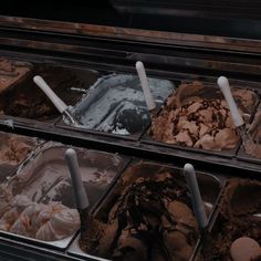 an assortment of ice creams in trays with spoons on top and chocolate