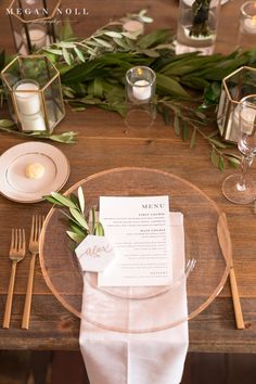 a place setting with napkins, silverware and greenery on a wooden table