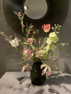 a vase filled with flowers sitting on top of a table next to a round mirror