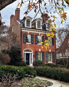 a large brick house with black shutters on the front and side windows, surrounded by greenery