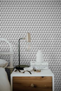 a nightstand with a lamp and books on top of it next to a wallpaper