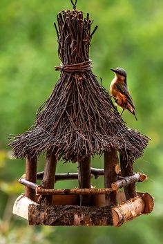 a bird is perched on top of a small house made out of sticks and twigs