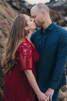 an engaged couple kissing on the beach in front of some rocks during their engagement session