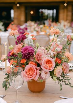 Lush arrangement features soft pink roses, magenta dahlias, and coral carnations, complemented with delicate greenery in a terracotta pot. Rustic elegance for a charming outdoor table setting. Peach And Pink Centerpieces, Pink Floral Table Arrangements, Terracotta Floral Arrangement, Terracotta Flowers Wedding, Terracotta And Pink Wedding, Pink Maroon Wedding, Terracotta Wedding Table Settings, Coral Carnations, Dahlia Centerpiece Wedding