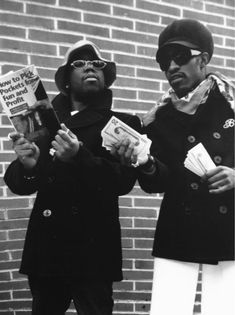 two young men standing next to each other holding papers and money in their hands,