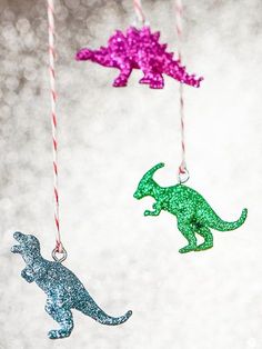 three glitter dinosaur ornaments hanging from twine with pink and green string attached to them