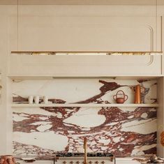 a kitchen with white cabinets and marble counter tops, gold accents on the backsplash