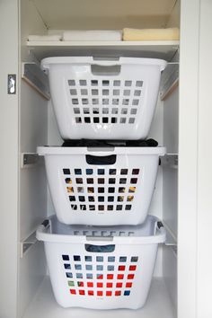 two white laundry baskets stacked on top of each other in an open cabinet with doors