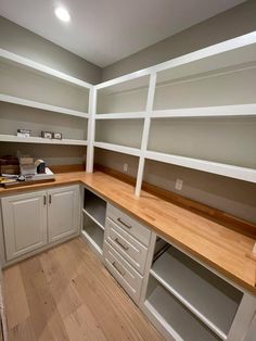 an empty kitchen with wooden counter tops and white cabinets, along with shelves on the wall