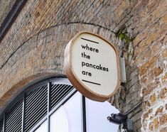 there is a sign that says where the pancakes are hanging from the side of a brick building