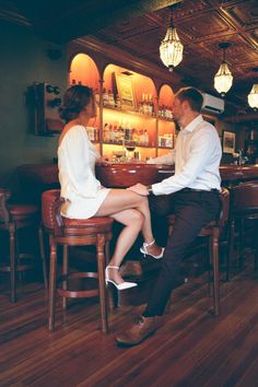 a man and woman sitting at a bar with their feet on each other's legs