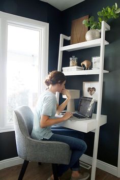 a woman sitting at a desk in front of a window with a laptop computer on it