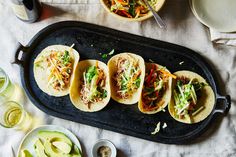 four tacos are lined up on a black tray