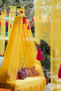 a yellow bed with red tassels hanging from it's sides and pillows on the floor