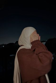 a woman in a brown and white hijab is covering her face with her hands