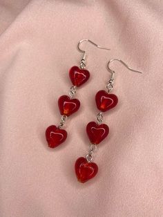 three red heart shaped glass beads hang from silver earwires on a pink cloth