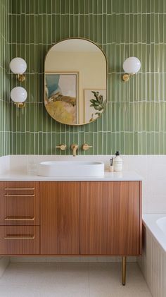 Elegant mid-century modern bathroom with Blu Dot-inspired elements, featuring a freestanding vanity in walnut wood with tapered legs and flat-front doors with brass pull handles, reminiscent of classic mid-century furniture. The countertop is a white quartz slab, paired with a modern, curved brass faucet for a touch of vintage charm. The bathtub area is wrapped in olive green subway tiles with a glossy finish, arranged in a stacked pattern to add a contemporary edge. Above the vanity, an arched mirror with a thick brass frame makes a statement, flanked by retro-inspired sconces with globe bulbs and brass accents. The floor is laid with terrazzo tiles in shades of cream and beige, adding texture and visual interest, while framed vintage artwork on the walls completes the space with a refine Bathroom Decor Mid Century Modern, Vintage Inspired Bathroom Vanity, Half Bathroom Ideas Mid Century Modern, Mid Century Coastal Bathroom, Bathroom Tile Mid Century Modern, Small Bathroom Ideas Mid Century Modern, Mid Century Modern Bathroom Green Tile, Mid Centric Modern Bathroom, Retro Small Bathroom