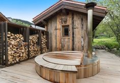 an outdoor hot tub next to a building with wood stacked on it's sides